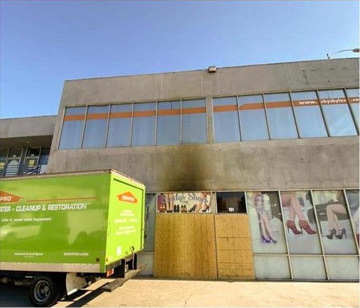 Exterior of a building, door boarded with plywood, green truck box parked